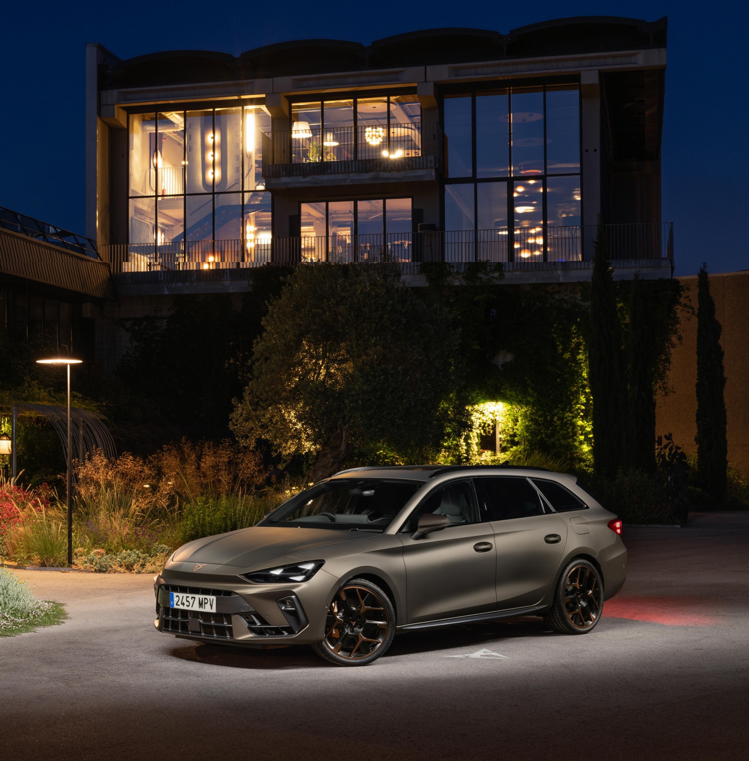 CUPRA Leon Sportstourer station wagon con design sportivo e cerchi color rame parcheggiata in un giardino moderno illuminato di notte.