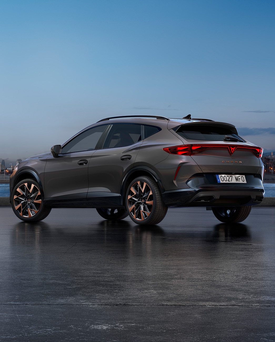 Una nuova CUPRA Formentor 2024 stile CUV con carrozzeria Grigio Grafene parcheggiata lungo un waterfront al crepuscolo. Lo sfondo presenta un paesaggio urbano con grattacieli e palme illuminati dalla luce del giorno che sta scemando.