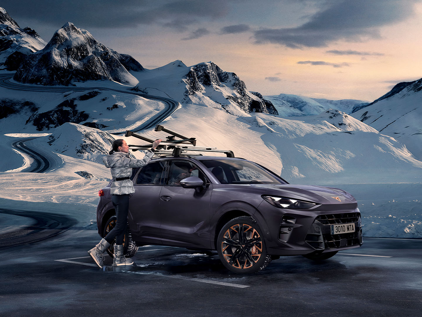 CUPRA Terramar in uno sfondo innevato, che mostra il portasci, uno dei suoi accessori di trasporto, assemblato sul tetto. C'è una donna che usa questo portasciliere per trasportare gli sci.