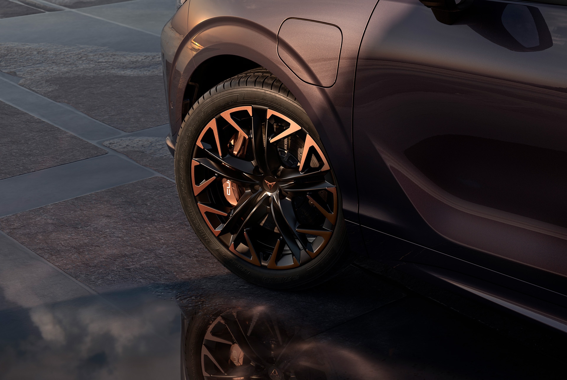 Cerchi in lega Hadron Copper da 20 pollici sulla nuova CUPRA Terramar, neri con dettagli in rame. Sullo sfondo si vedono un manto stradale piastrellato e parte della carrozzeria scura e lucida dell'auto.