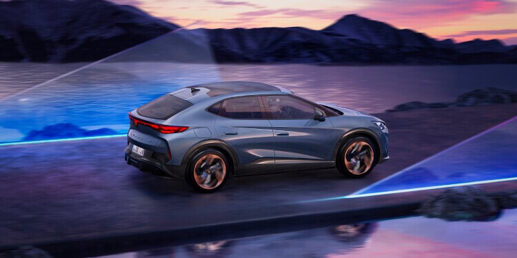 CUPRA Tavascan VZ 2025 in motion, 3/4 rear view, Tavascan Blue colour, driving through a mountainous landscape at sunset.